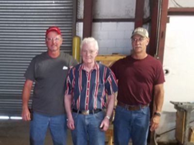 Three men standing together in a warehouse or workshop setting.