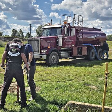 Two workers inspecting a hose by a large tanker truck.