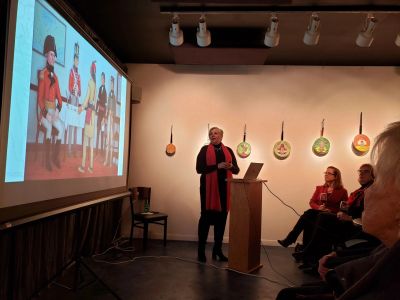A presenter speaks to an audience with historical images projected on a screen.