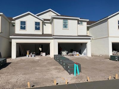 Newly constructed duplex with open garages and unfinished driveways under a clear sky.