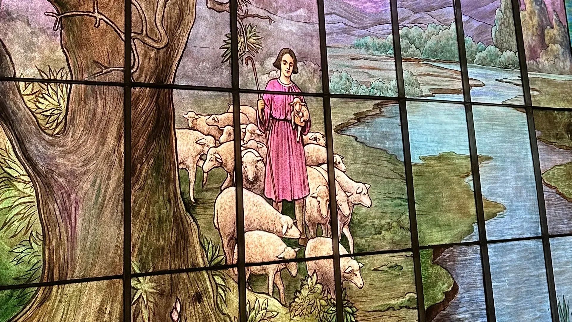 Church stained glass window of a shepherd guiding sheep by still waters.