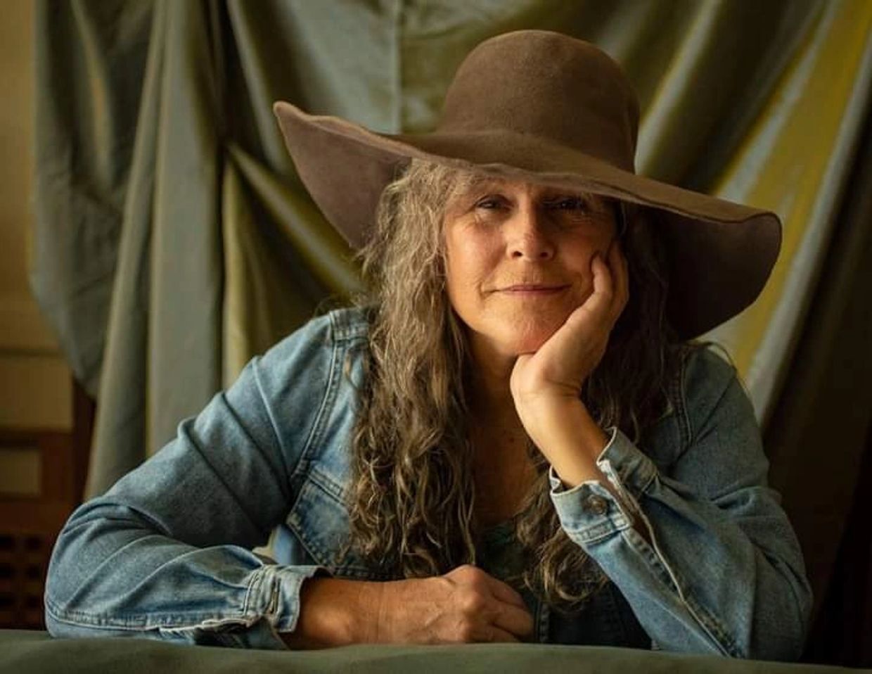 Woman with long gray hair wearing a wide-brimmed hat and denim jacket.