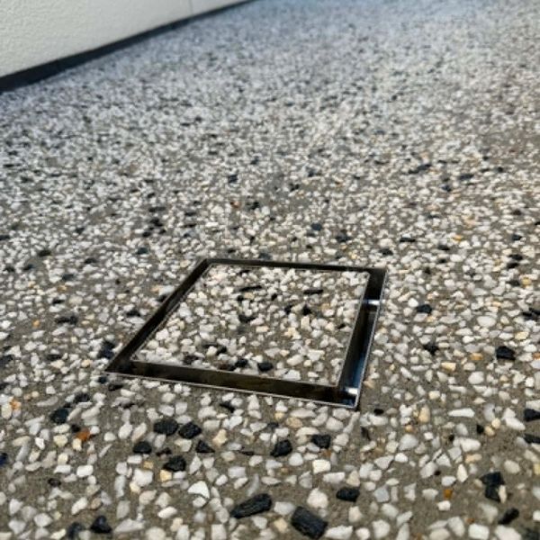 Square drain cover blending into textured stone floor.