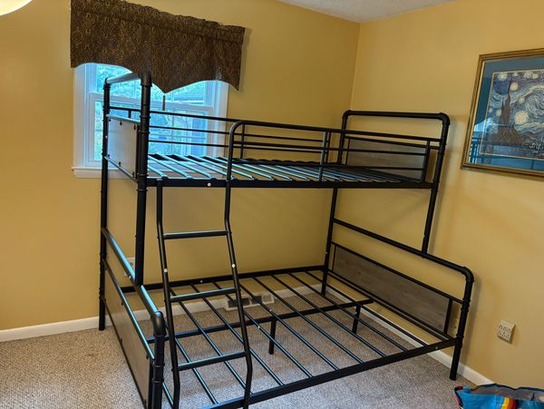 Black metal bunk bed frame in a yellow-walled bedroom with a window and framed artwork.