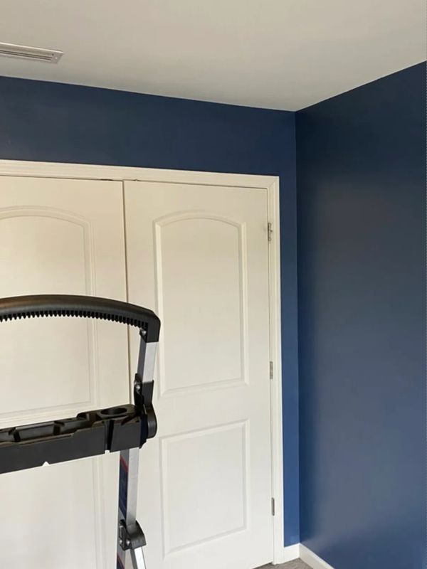 A blue-painted room corner with white closet doors and a foldable ladder.
