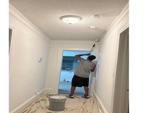 Person painting a hallway wall white using a roller brush.
