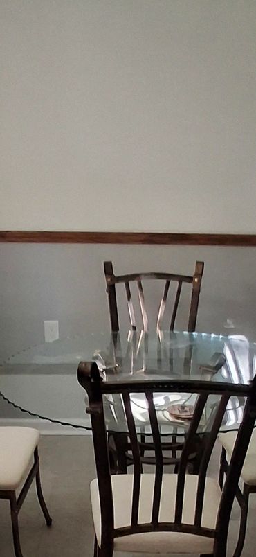 Kitchen dining area with glass table with chairs and natural light from window.