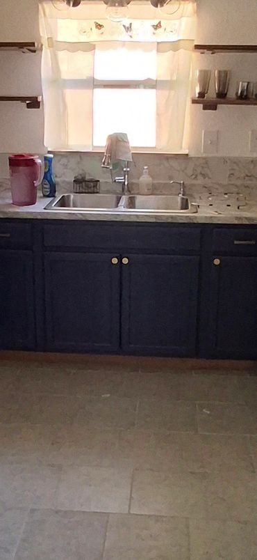 Full kitchen view with refrigerator, stove, sink window, countertops, and lower cabinet storage.