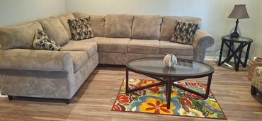 Cozy seating area with sectional couch, rug, table and front window view. Security cameras in place.