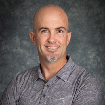 Smiling bald man in a patterned gray shirt against a textured backdrop.