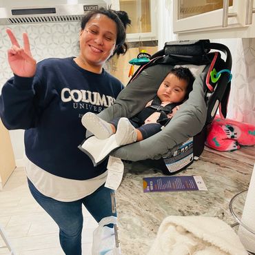 Parenting Plus client with peace sign and baby asleep in a car seat in the main Parening Plus campus.