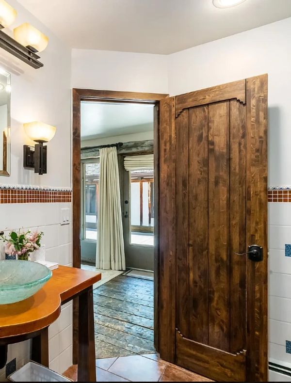 Rustic wooden door opens to a room with large windows and curtains.