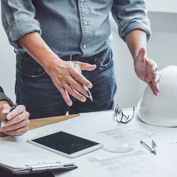 A man wearing a blue shirt standing over a desk gesturing about a design to another person.