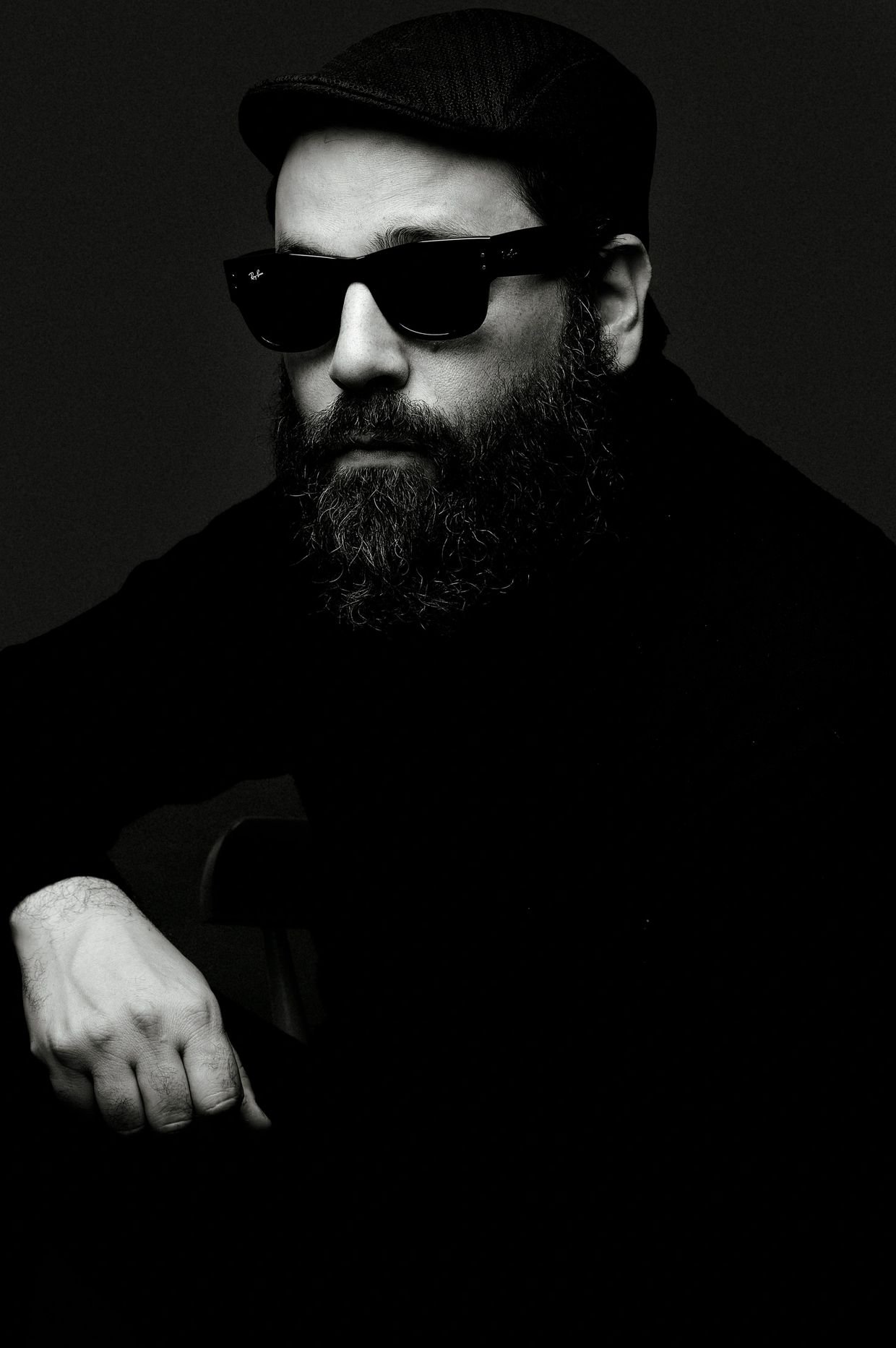 Homem com óculos escuros e barba, vestindo boné.