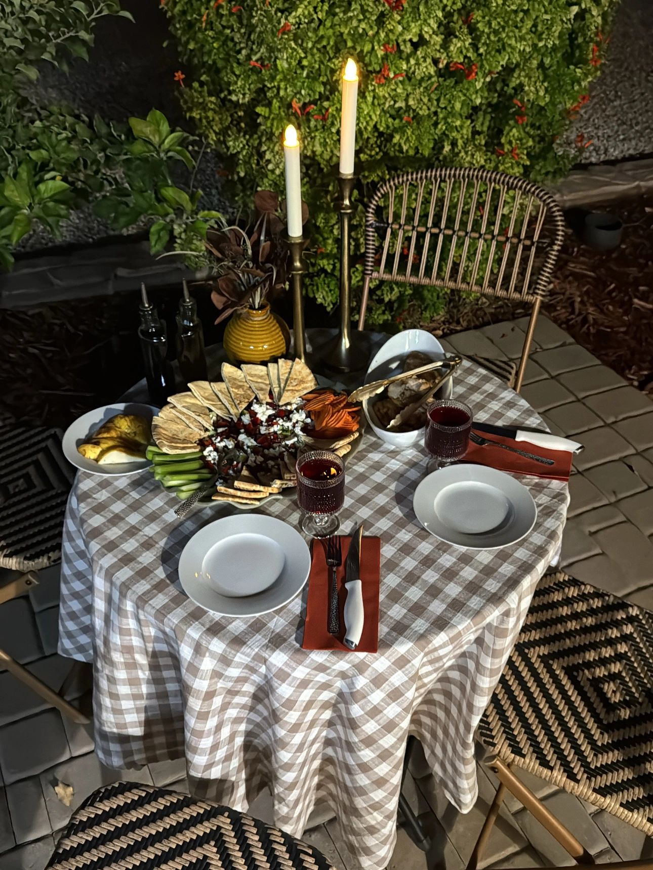 Cozy outdoor dinner setup with candles and snacks on a checkered tablecloth.
