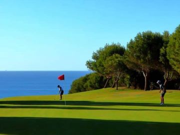 golf green with player putting and ocena in the background.