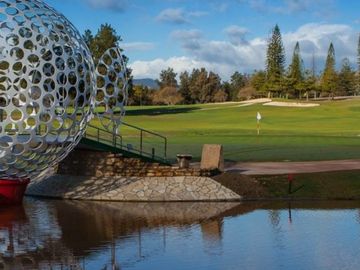 golf course with large golf ball art structure to the left and beyond the green with a white flag.