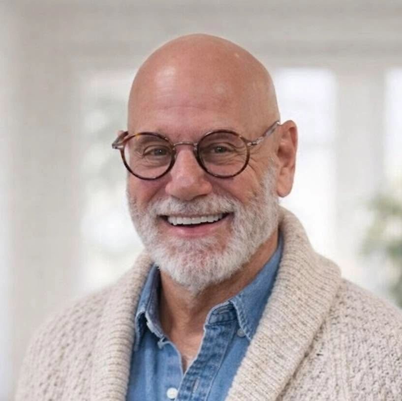 Smiling elderly man with glasses and a white beard, wearing a cozy sweater.