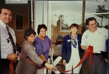 Group of people cutting a red ribbon at an event.