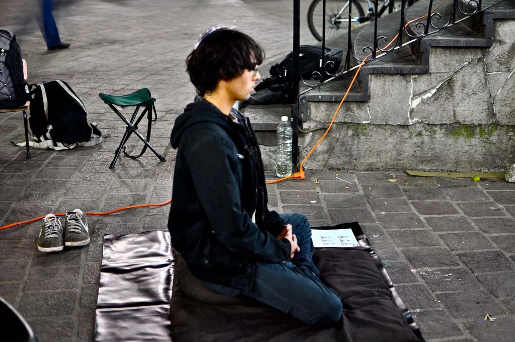 A man meditating outdoors on a mat with shoes off nearby.