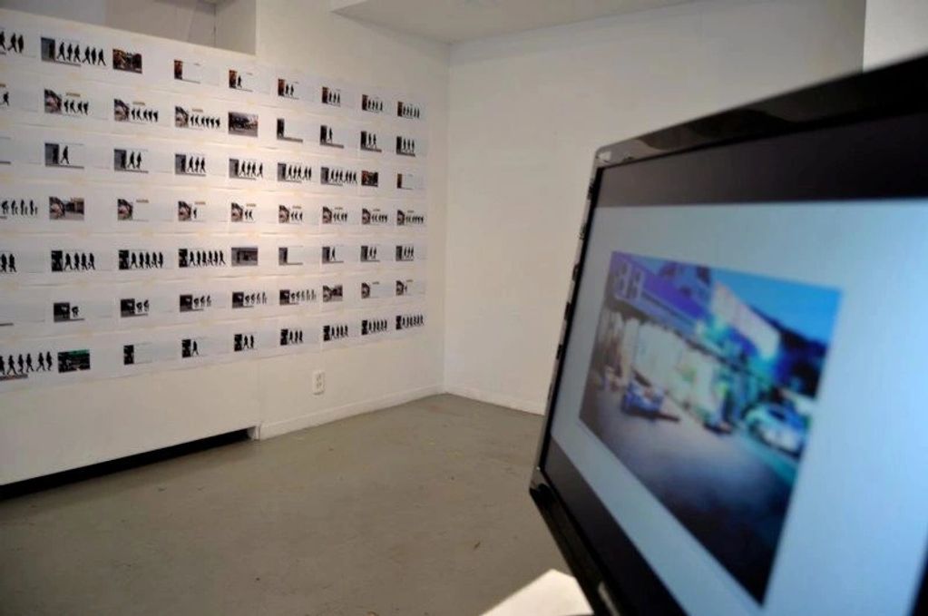 Gallery room with a wall of photos and a blurry screen display.