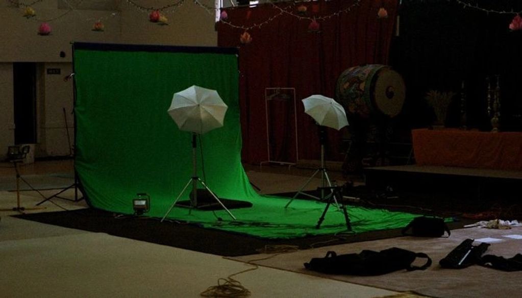 Indoor photo studio setup with green screen and lighting umbrellas.