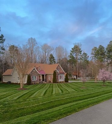 A charming house with a beautifully striped lawn and blossoming trees under a blue sky.