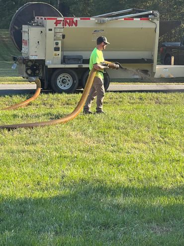 Worker operating a Finn machine spreading material on a grassy area.