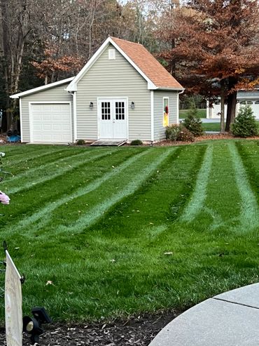 Freshly mowed lawn with striped patterns leading to a small beige garage.