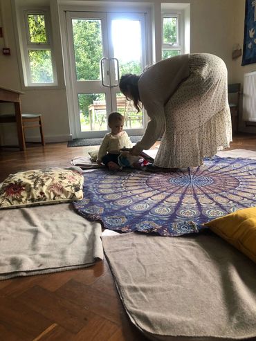 A woman leans down holding a toy out for a small child during a Mother & Baby Circle in Bristol