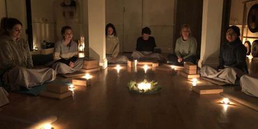 Women gather in a circle lit up by candles with a centrepiece, hosted by a Doula in Bath