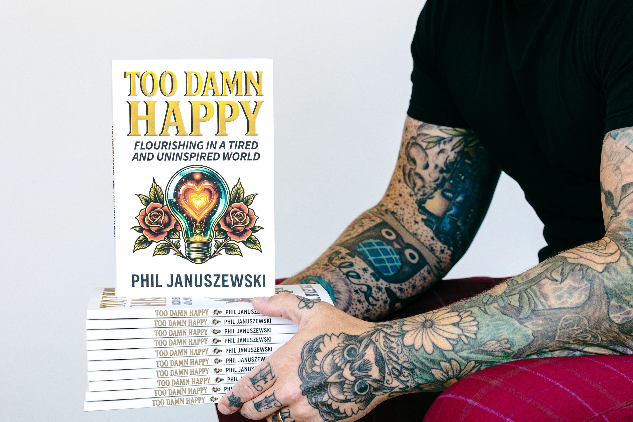 Stacked copies of Too Damn Happy by author and keynote speaker Phil Januszewski, a personal developm