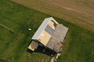 Aerial view of an old barn with a partially repaired roof in a green field.
