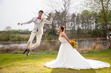 A bride and groom jumping for joy beside the lake outside our barn wedding venue.