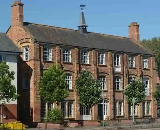 Historic brick building with large windows and greenery in front.