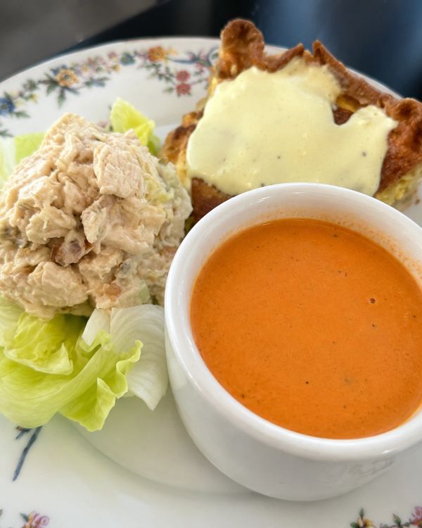 Plate with creamy soup, chicken salad on lettuce, and a slice of quiche with cheese.