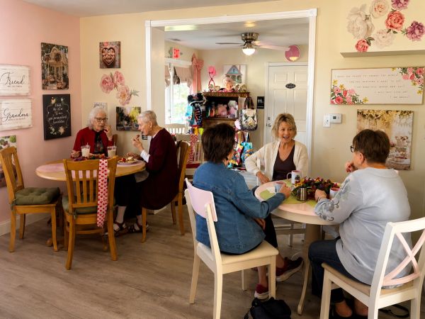 Two pairs of elderly women enjoying conversation and snacks in a cozy, decorated room.