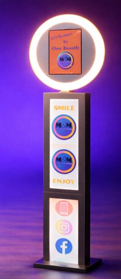 Photo booth setup with a glowing ring light and social media icons on a stand.