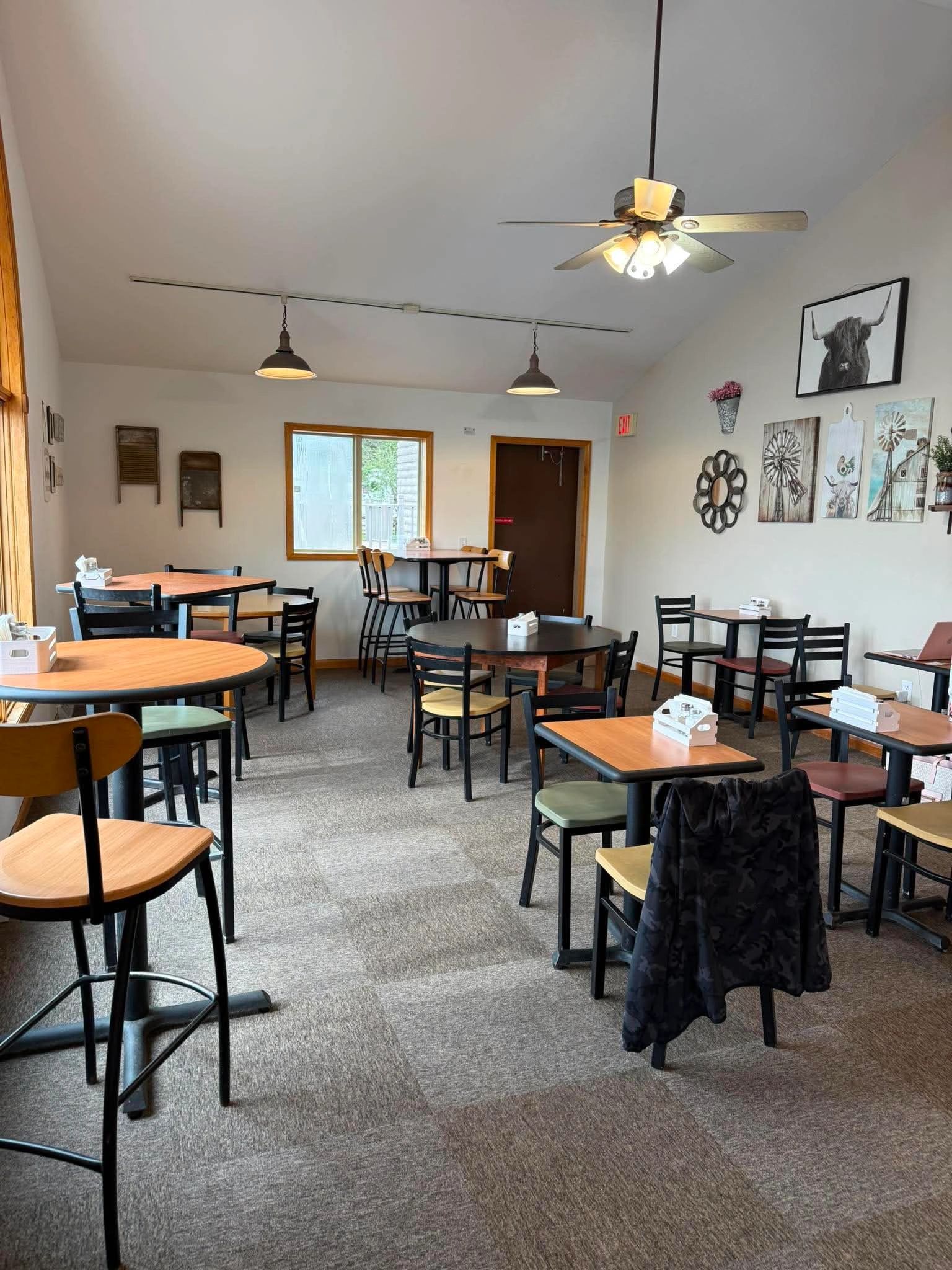 Cozy cafe interior with wooden tables and chairs, decorated with rustic wall art and a ceiling fan.