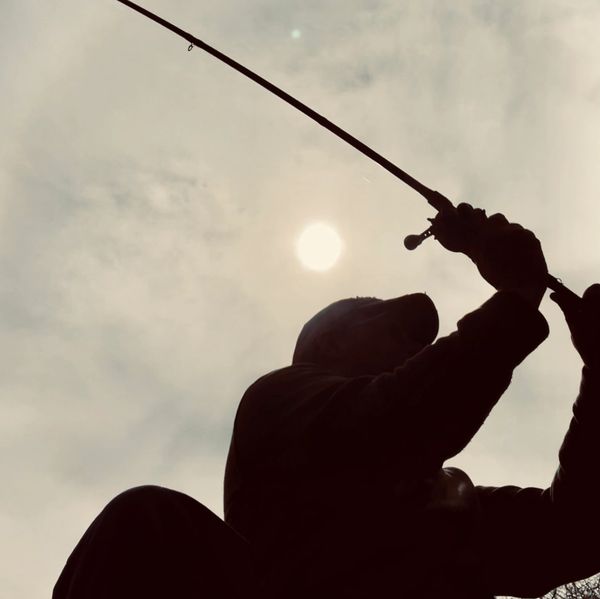Silhouette of a person fishing with the sun behind.