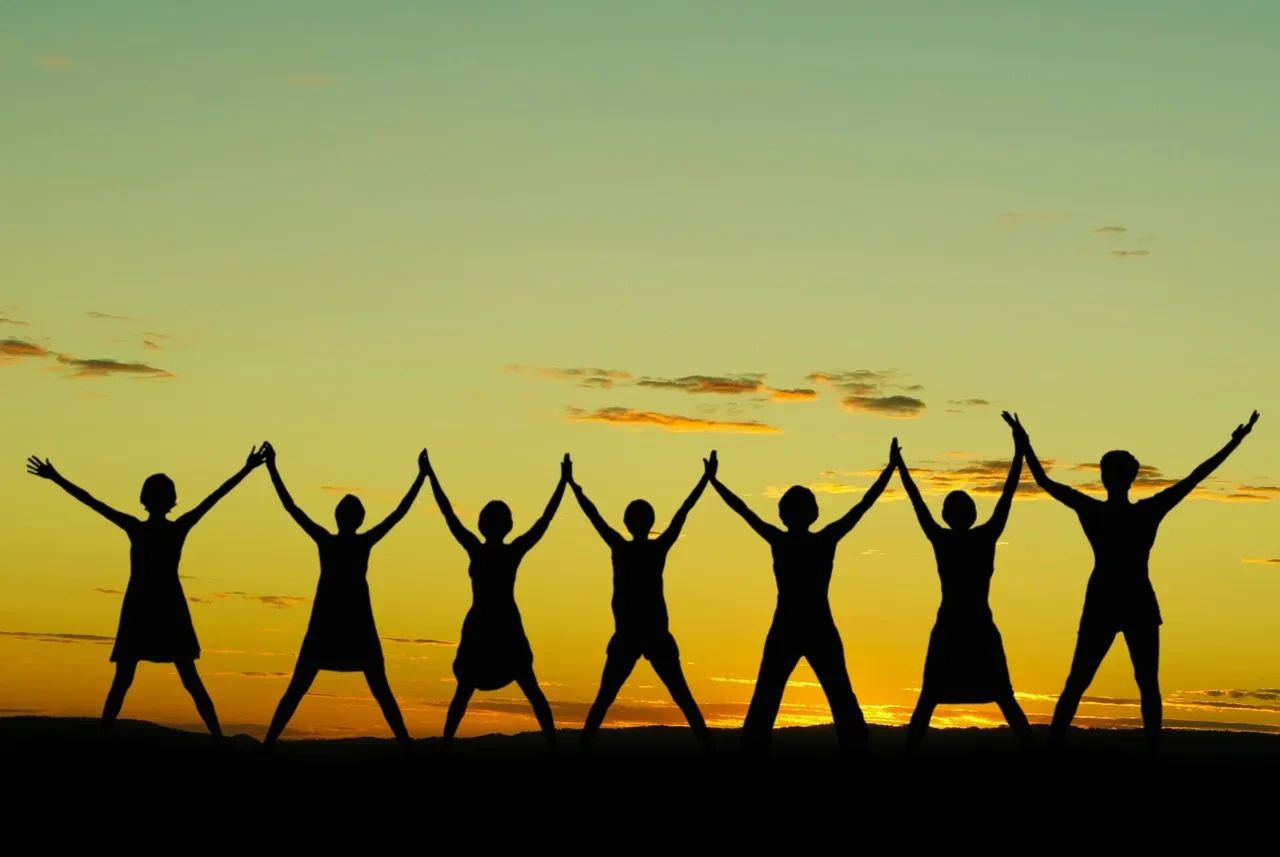 Group holding hands with raised arms at sunset.