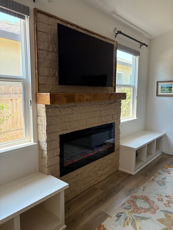 Modern living room with stone fireplace and mounted TV between two windows.