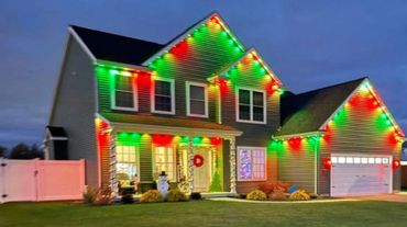 Two-story house decorated with green and red Christmas lights.