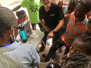Joe demonstrates the Rescuer by purifying the water that a Haitian man's foot is in.