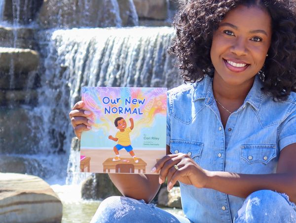 Image of Cori Riley, author of "Our New Normal" holding the children's book while sitting outside.
