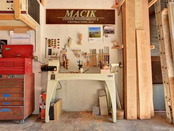 Organized woodworking shop with lathe, tools, and wood planks under a custom woodworking sign.