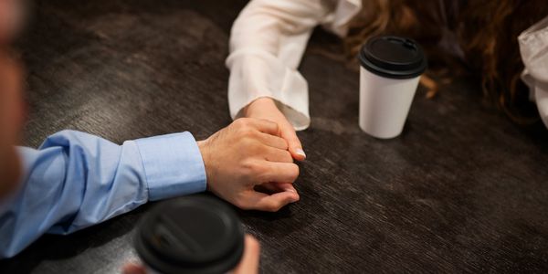 Friends holding hands across a table with coffee cups.