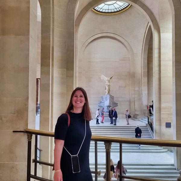 Flora is a Louvre Guide standing in front of the Winged Victory