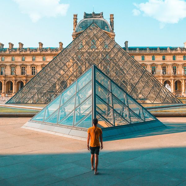 Man standing in front of the pyramid of Glass of the Louvre