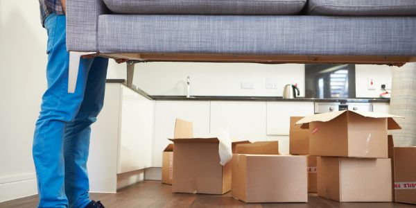Person moving a couch with unpacked boxes around.